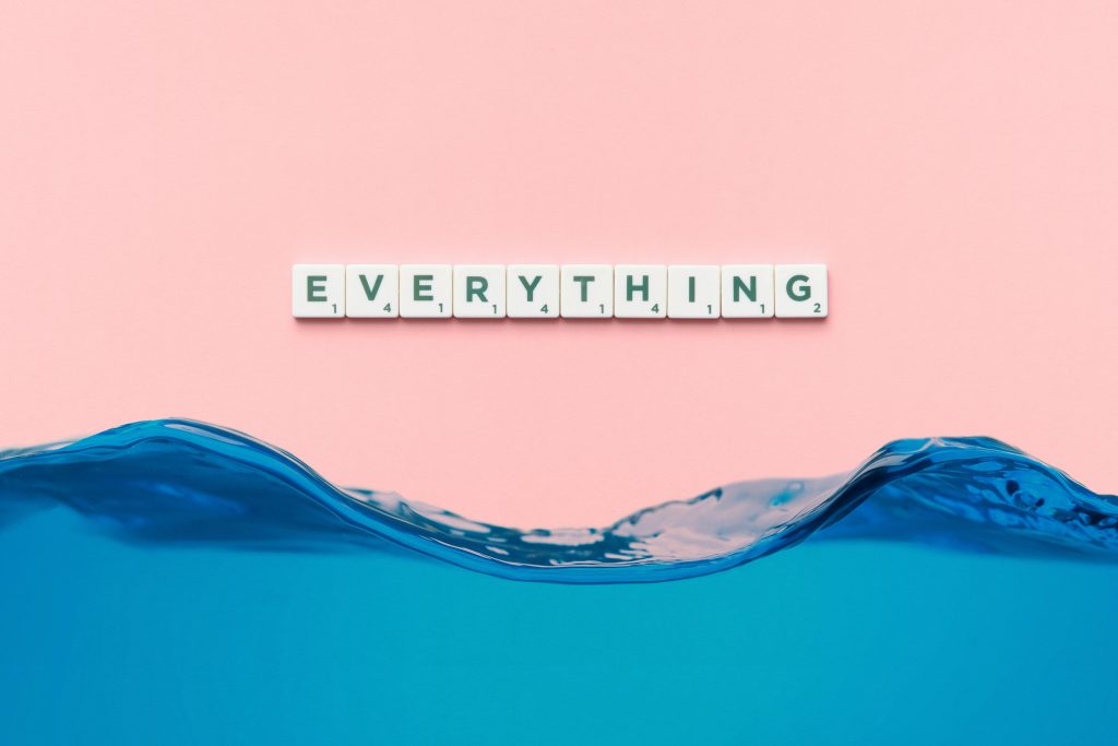 Scrabble tiles spelling 'everything' float above a blue wave on a pink background.